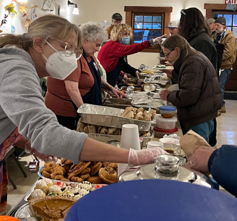 volunteers serve food to people lined up.